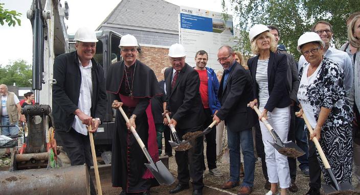 Menschen mit einem Spaten in der Hand stehen zusammen und eröffnen die Baustelle am Bürgerzentrum