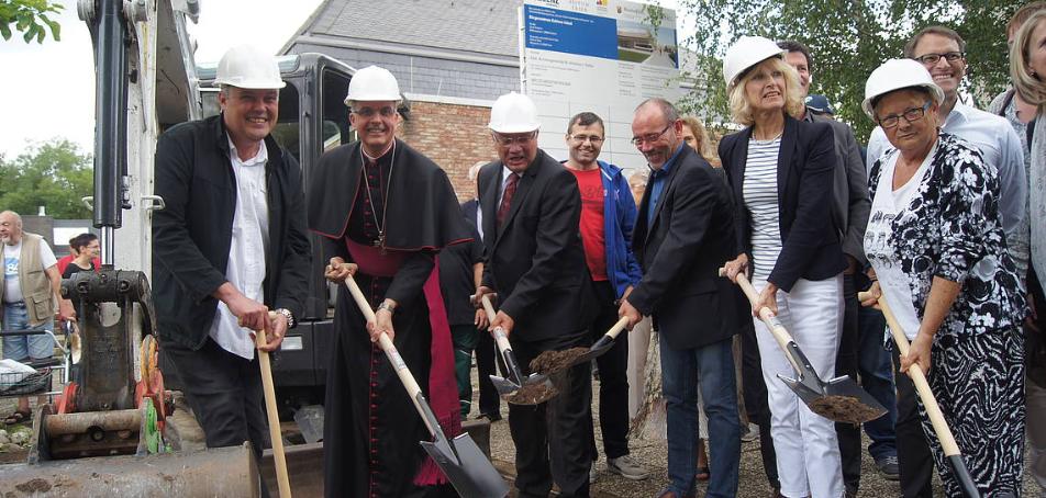 Menschen mit einem Spaten in der Hand stehen zusammen und eröffnen die Baustelle am Bürgerzentrum