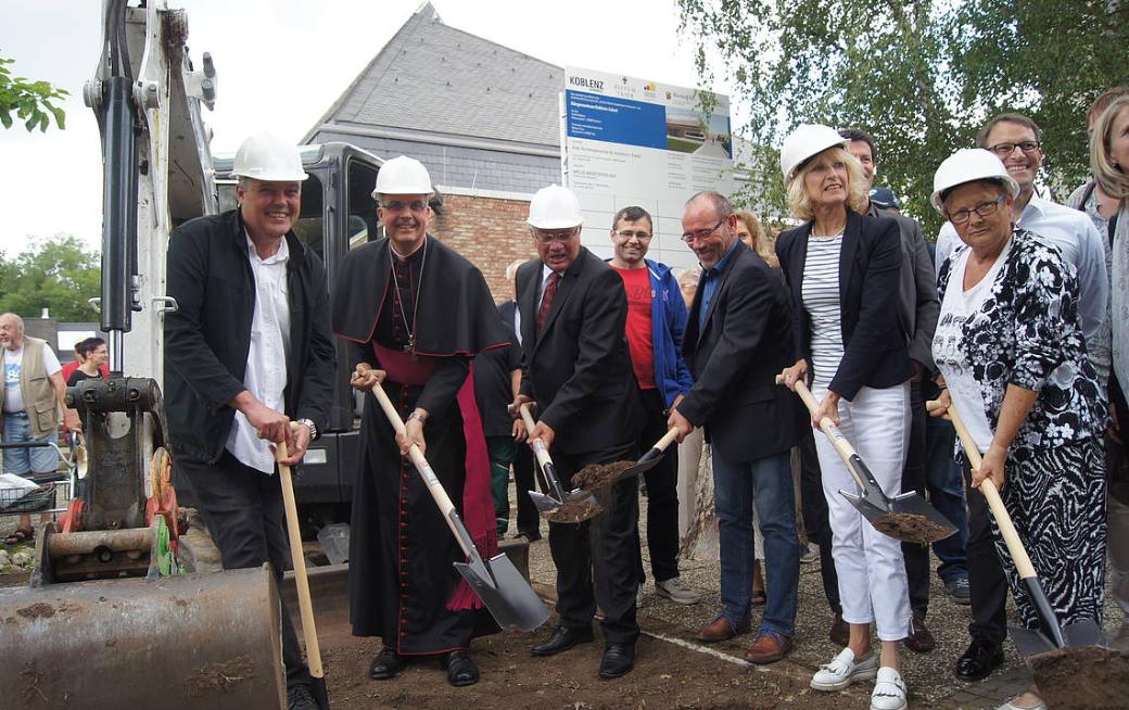 Menschen mit einem Spaten in der Hand stehen zusammen und eröffnen die Baustelle am Bürgerzentrum